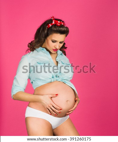 Pin up retro styled studio shot of a surprised pregnant woman. Photograph taken in studio on a pink, vibrant background with copy space.