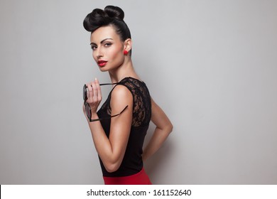 Pin Up Style Woman Holding Round Sunglasses Posing In Red Skirt. Red Lips. Updo, Twisted High Bun. Top Knot