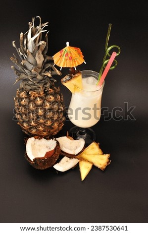 Pina Colada, a tall glass with a refreshing iced cocktail on a black background, next to a ripe pineapple and a broken coconut. Close-up.