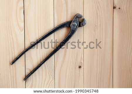 Pincers, tool for removing nails from wood. Vintage metal nippers on a light wooden background. Old open rusty pinching pliers to used for removing nails from wood.