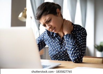 Pinched nerves, tensed sore muscles, fibromyalgia ache due sedentary lifestyle and incorrect posture concept. Indian ethnicity frowning woman sitting at desk in front of laptop, touch neck feels pain - Shutterstock ID 1835827765