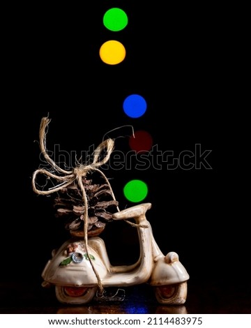 A pine cone tied with string to a model scooter with colored lights with bokeh effect in the background