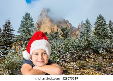  Pine forest in mountains are covered with the first snow. Charming eight-year boy in Santa Claus hat smiling