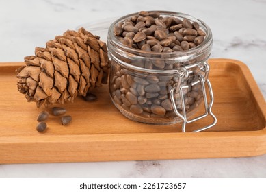 Pine nuts in a jar and a pine cone in the kitchen on a light background. The concept of organic food and protein food