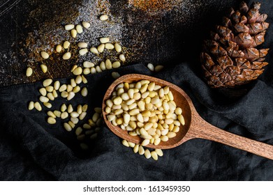 Pine nuts in the spoon and pine nut cone. Organic food. Black background. Top view