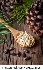 Pine nuts in the spoon and pine nut cone on the wooden table. Organic food.