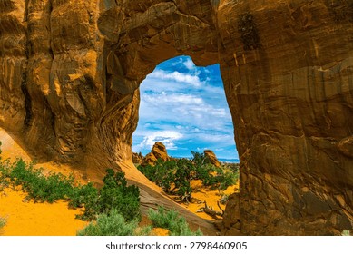 Pine Tree Arch frames a vivid view of sandstone hoodoos, junipers, and blue sky beyond, Devils Garden, Arches National Park, Utah.