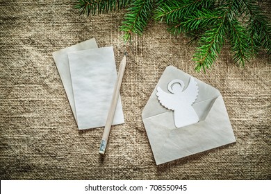 Pine tree branch envelope letter pencil angel on sacking background.