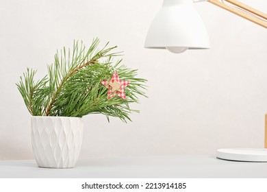 Pine Tree Branch In White Vase On Table Top Next To Desk Lamp. Minimal Christmas Home Decor, Winter Holiday Office Decor. Copy Space