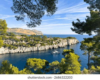 Pine trees framing a boat navigating the clear blue waters of calanque d'en vau