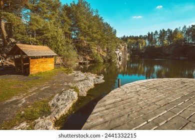 Pine trees on the lakeshore. Serene lake with wooden small fishing house. Wooden round pier on the lake. Nature landscape.  - Powered by Shutterstock