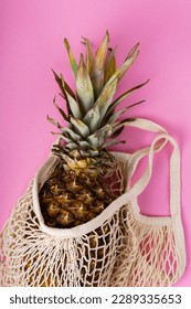 pineapple in a beige string bag on pink background
