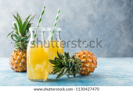 Pineapple cocktail or juice in two glass bottles with straws with ice and two mini pineapples on a blue background
