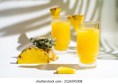 Pineapple cocktail or juice in two glasses with ice on white background with palm leaves shadows