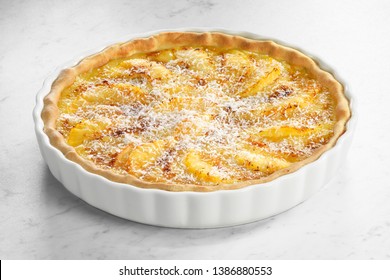 Pineapple and coconut tart in a white pie dish on white marble background