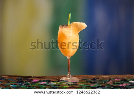 Pineapple drink to refresh in the summer. Glass with ice, over wooden balcony decorated for carnival, with beach scenery in the background