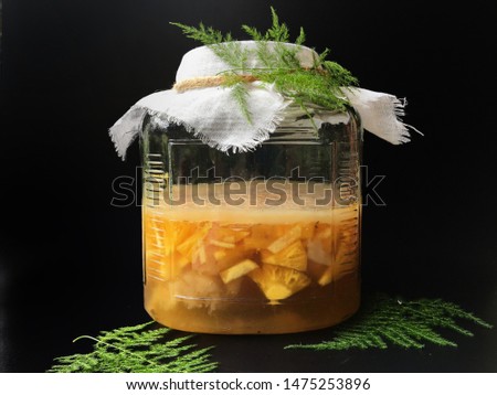 Pineapple fermentation with sugar and water in glass bottle  for kombucha tea, black background.