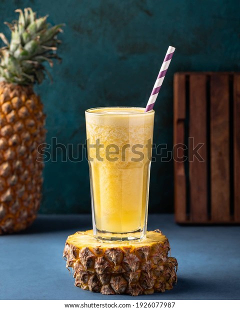 Pineapple juice in a glass\
with straw on a pineapple piece with a pineapple beside it ,\
Selective focus