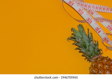 Pineapple Lying On A Mustard Background With A Measuring Tape - The Concept Of Healthy Weight Loss, Selective Focus