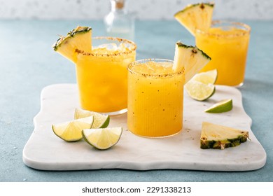 Pineapple margarita cocktail in glasses with chili tajin rim and a slice of pineapple, refreshing summer cocktail