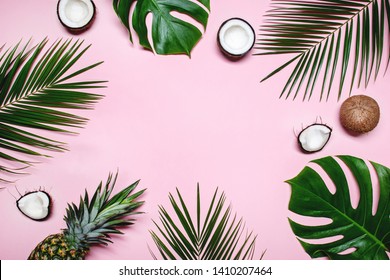 Pineapple, ripe coconuts, tropical palm and green monstera leaves on pink background.