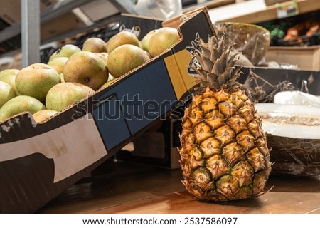 A pineapple sits on a table next to a cardboard box that says 