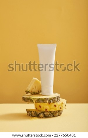Pineapple slices with round shape are stacked and a white tube with empty label putted on top. Product mockup with pineapple (Ananas comosus) extract