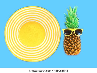 Pineapple With Sunglasses And Yellow Straw Beach Hat On Blue Background Top View