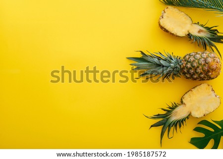 Pineapples and palm leaves on yellow color summer background. Whole tropical summer pineapples fruits and sliced pineapple halves flat lay composition with copy space