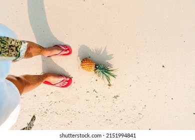  pineapples and red flip flops on the beach.