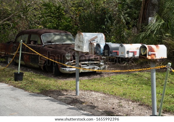Pinecrest,\
Florida/USA -February 2,2020 : Mailboxes at Pinecrest along the\
Loop Road.A creepy doll is propped on the seat of an abandoned\
rusty 1954 Dodge car in th\
ebackground