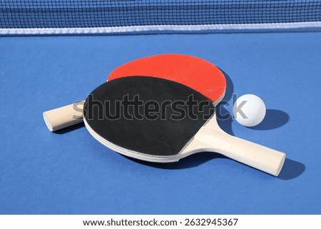 Ping pong rackets, ball and net on blue background, closeup