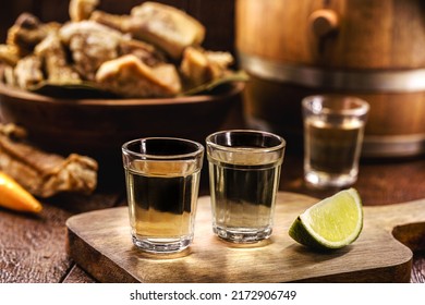 Cachaça, pinga, cana or caninha is the sugar cane brandy, a typical drink from Brazil, with a crackling appetizer in the background - Shutterstock ID 2172906749