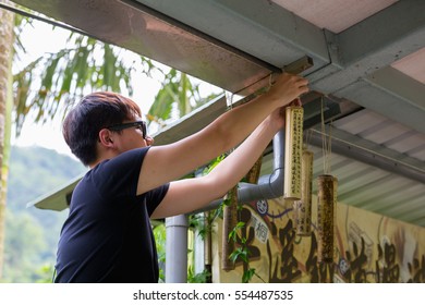 Pingxi, Taiwan - May 6, 2016:Man Hanging wishes on bamboo sticks hanging next to train station in Pingxi