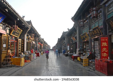 Pingyao, Shanxi, China - Nov 28 2018: A Main Street In Pingyao Lined With Small Shops And Stores. A Woman Is Cycling And People Are Walking. Pingyao Old Town Is A Famous Ancient Walled City In China.