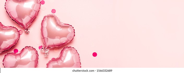 Pink air balloons in the shape of a heart on a pink background. Concept for Valentine's day, decoration, wedding, invitation or photo zone. Foil balls. Banner. Flat lay, top view