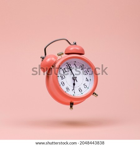 The pink alarm clock is levitate in the air, against pink background. The concept of time, copy space.