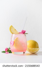 Pink Alcoholic Rose Beverage Or Lemonade, Cocktail With Rose Flowers And Lemon On White Sunny Background. Close Up. Vertical Format.