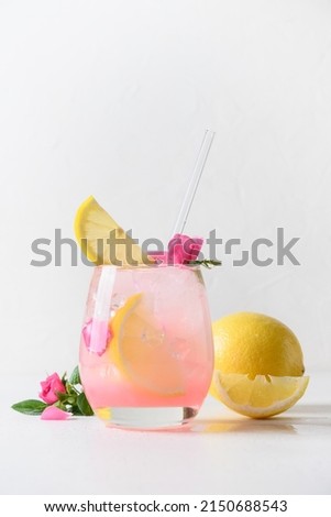 Pink alcoholic rose beverage or lemonade, cocktail with rose flowers and lemon on white sunny background. Close up. Vertical format.