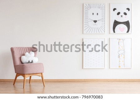 Pink armchair with cloud shaped toy standing in baby room with simple posters on empty wall
