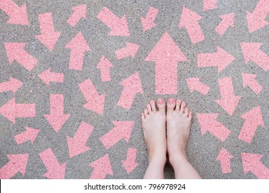 Pink Arrow Choice Concept. Female Bare Feet with Pink Nail Polish Manicure Standing and Many Direction Arrows Choices on the Road Background Great for Any Use.