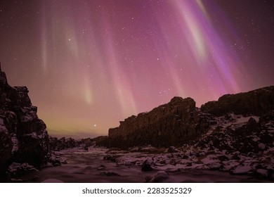 Pink aurora borealis over rocky river gorge, Thingvellir Iceland - Powered by Shutterstock