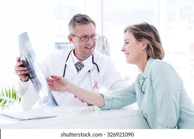 Pink awareness ribbon against doctor having conversation with his patient and holding xray