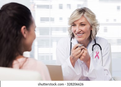 Pink awareness ribbon against friendly female doctor in conversation with patient