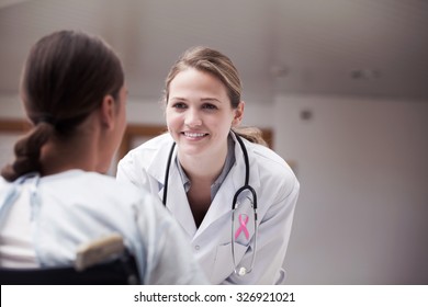Pink awareness ribbon against smiling doctor looking at a patient on a wheelchair