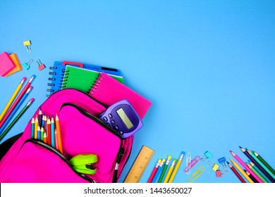 Pink backpack with corner border of school supplies against a blue paper background. Top view with copy space.