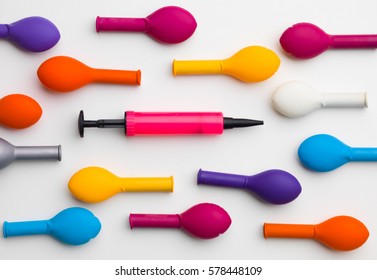 pink balloon pump between  colorful deflated balloons,  on a grey background
