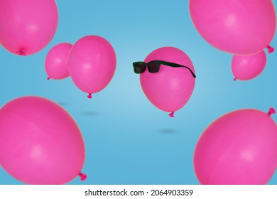Pink balloon in sunglasses floating in the air with other balloons against blue background. Minimal Creativity and happiness concept. Fun Party Mood, be different.
