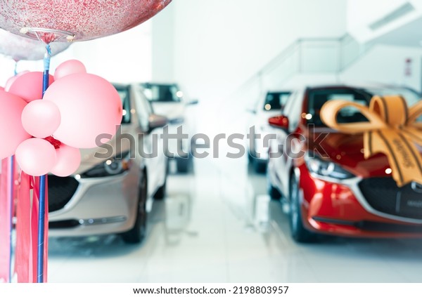 Pink balloons on blur car parked in luxury\
showroom. New car parked in modern showroom. Car dealership office.\
Automobile leasing and insurance concept. Auto leasing business.\
Electric vehicle dealer.