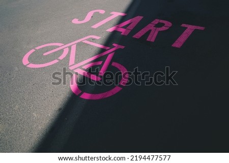 pink bicycle symbol with lettering start painted on inner city asphalt surface. urban mobility and woman sport motivation concept. slogan for ecological traffic turn. selective focus
